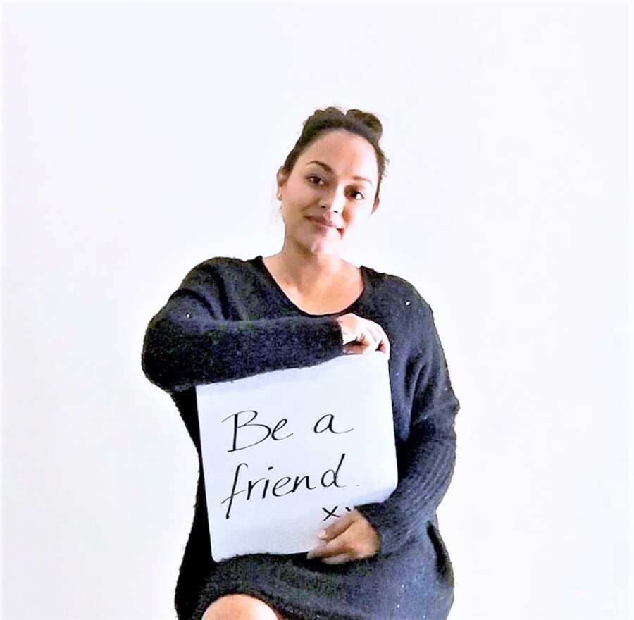 Mom victim of childhood bullying holding a sign saying "Be a friend"