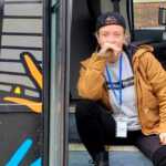 queer sober mom smiling while sitting on bus steps