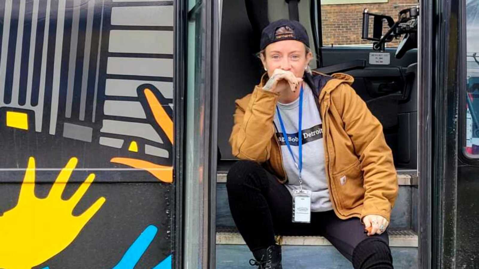 queer sober mom smiling while sitting on bus steps