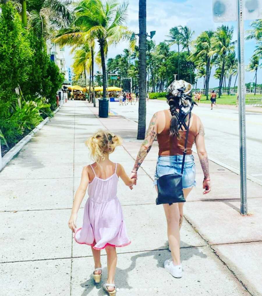 sober mom walking along sidewalk with daughter beside greenery