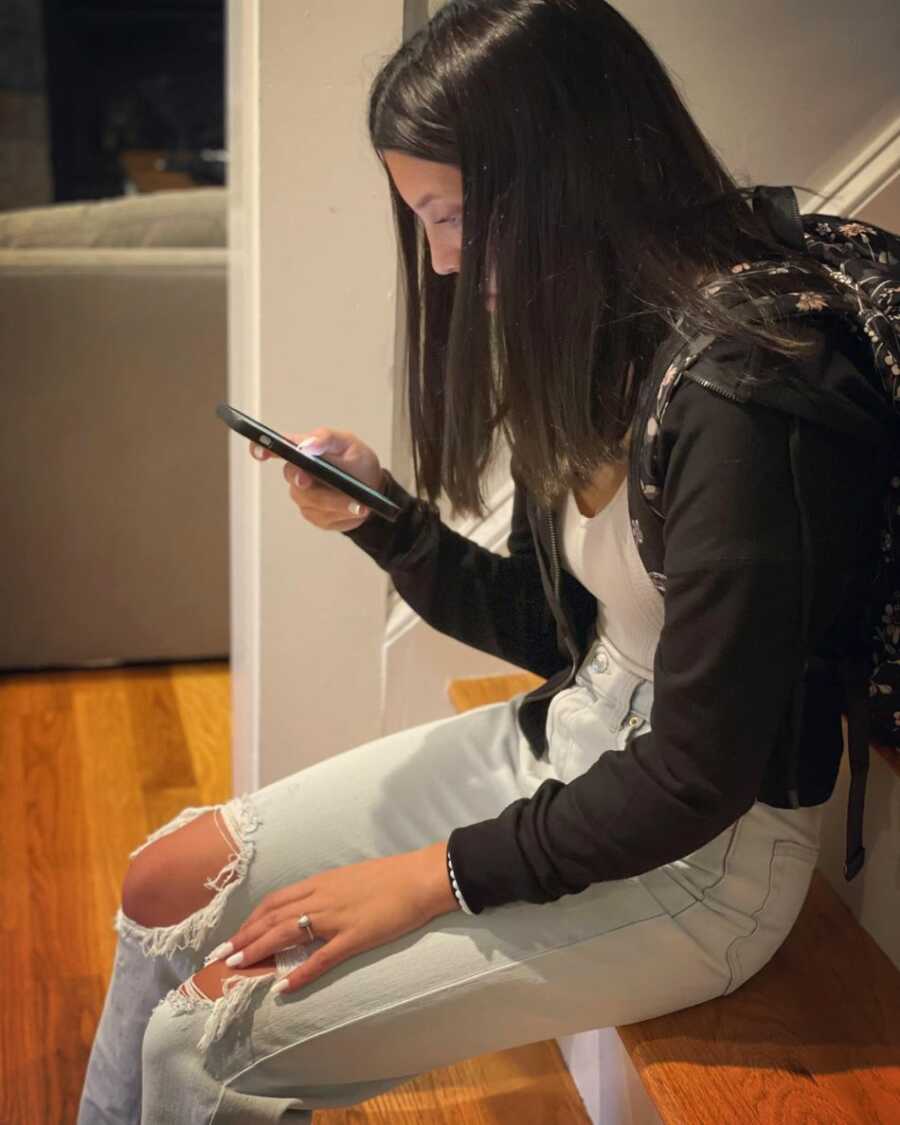 Daughter staring at iphone while sitting on stairs with backpack on