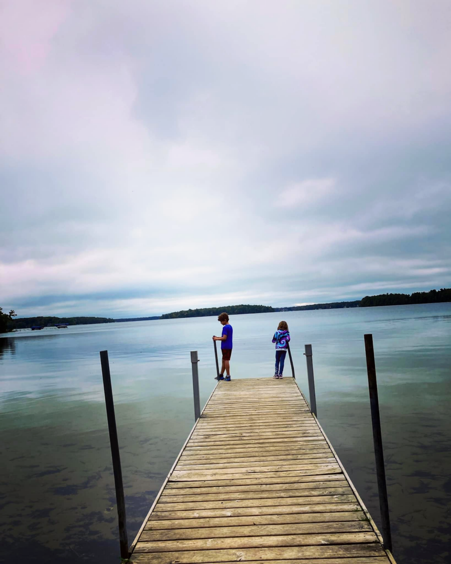 two kids standing on the end of the pier over a lake