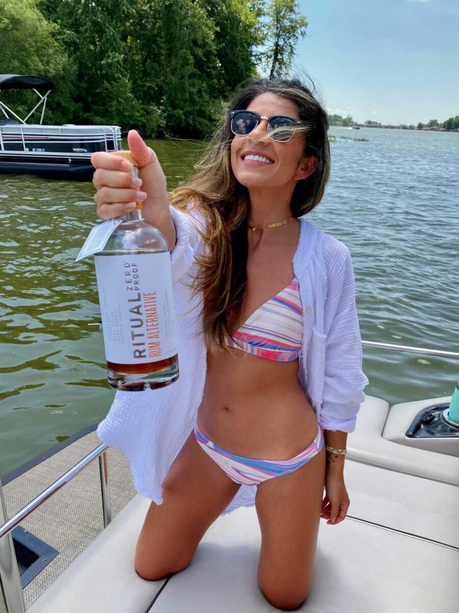 sober young woman wearing bikini holding alcohol alternative bottle on a boat
