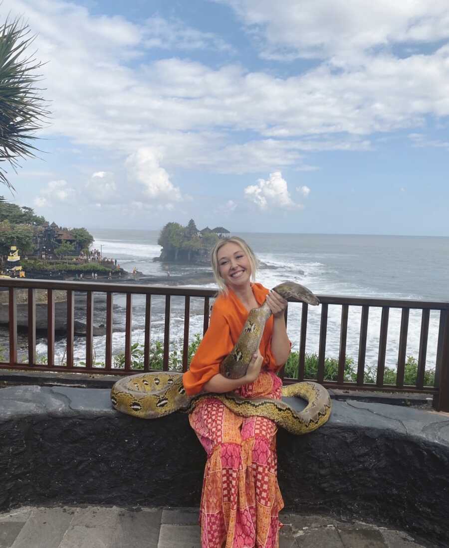 woman holds snake while in front of beach