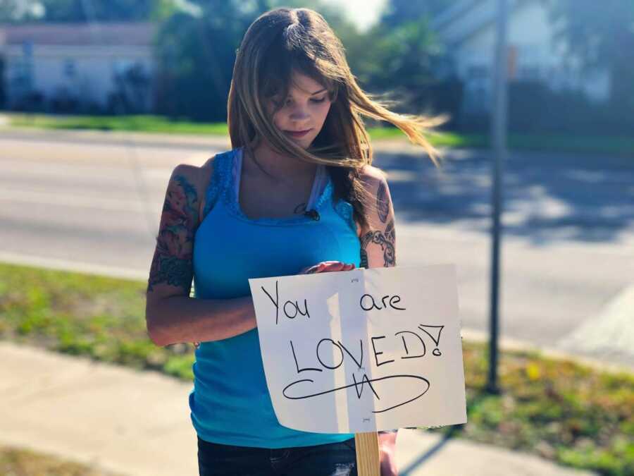 suicide attempt survivor wearing blue shirt holding a you are loved sign