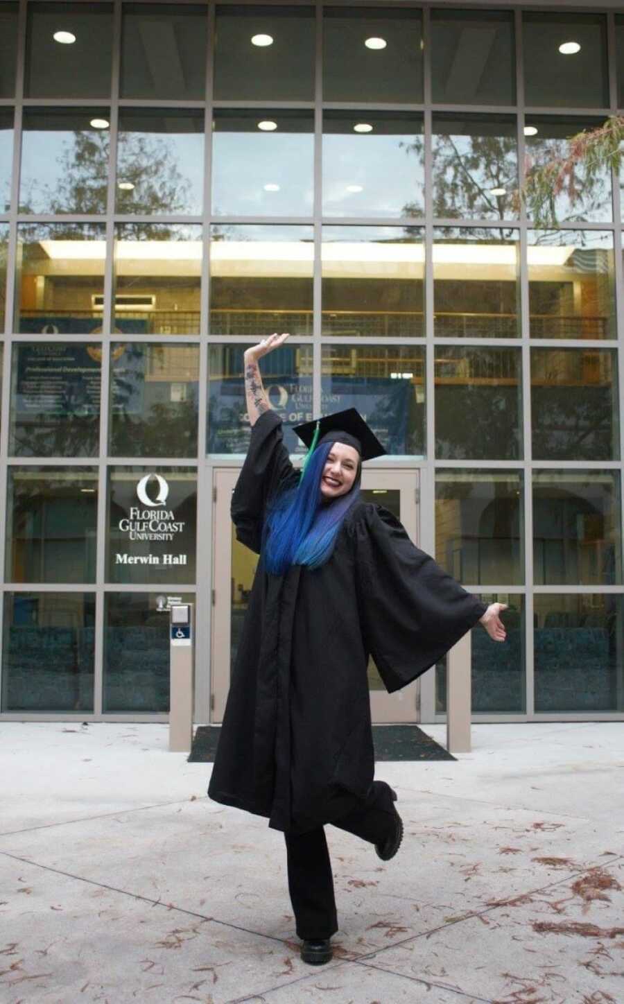domestic abuse survivor wearing graduation cap and gown in front of school
