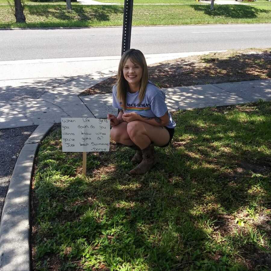 suicide attempt survivor squatting next to mental health awareness sign