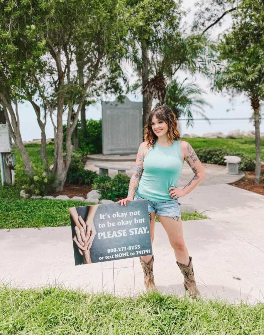 suicide attempt survivor in blue shirt standing next to mental health awareness sign