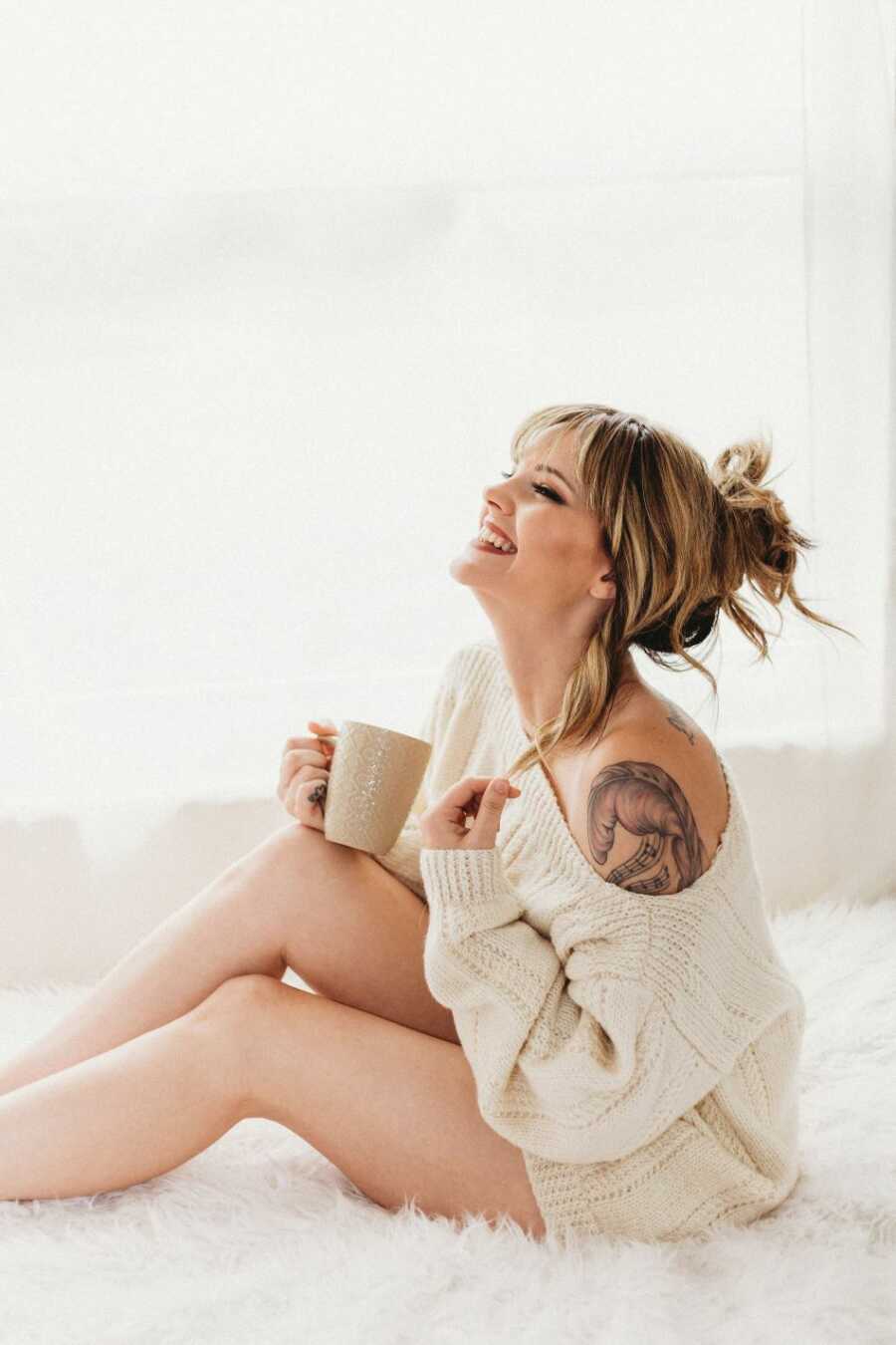 domestic violence survivor smiling wearing cream sweater holding coffee mug