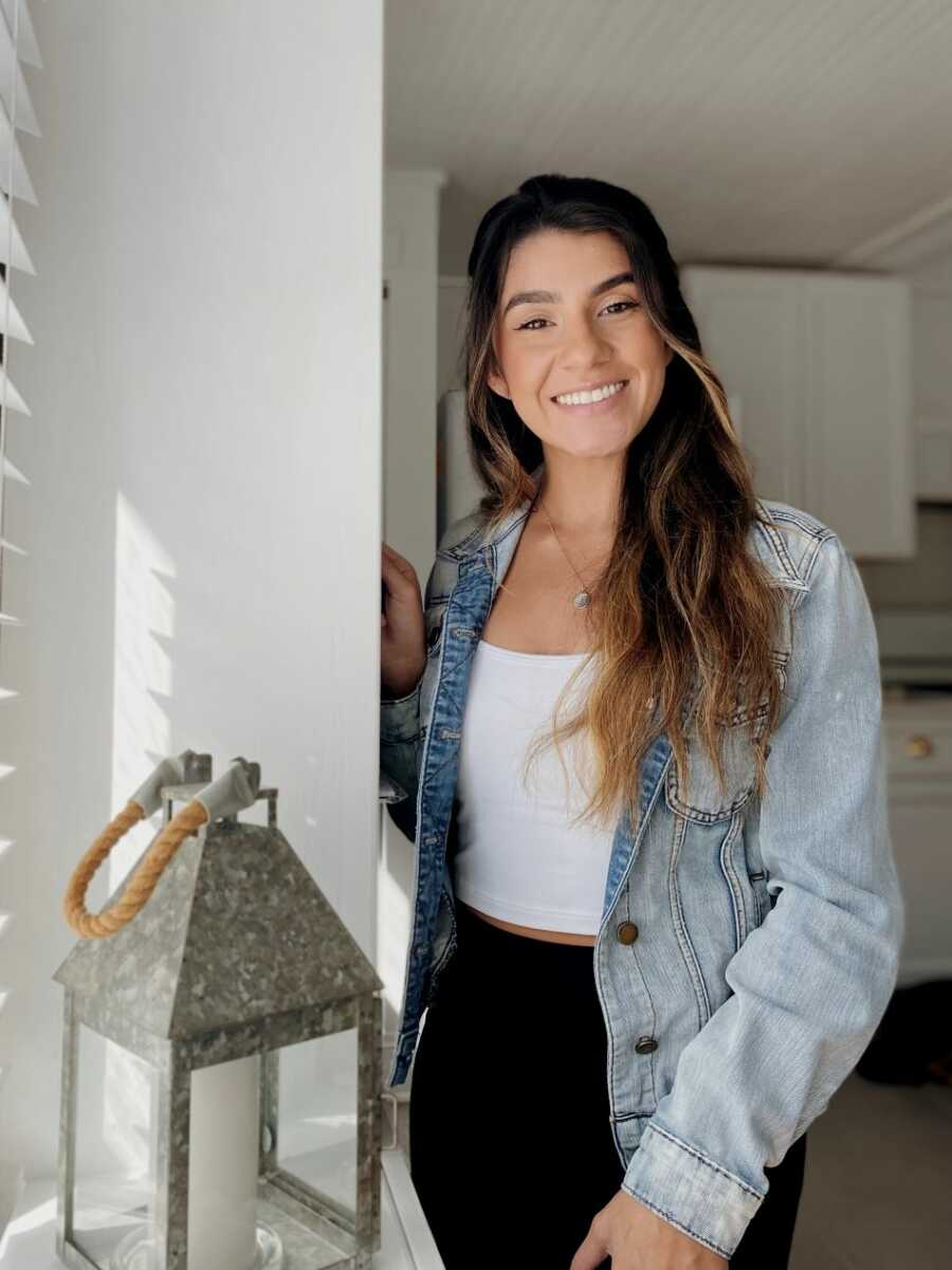 sober young woman wearing jean jacket and white shirt posing at camera next to white wall