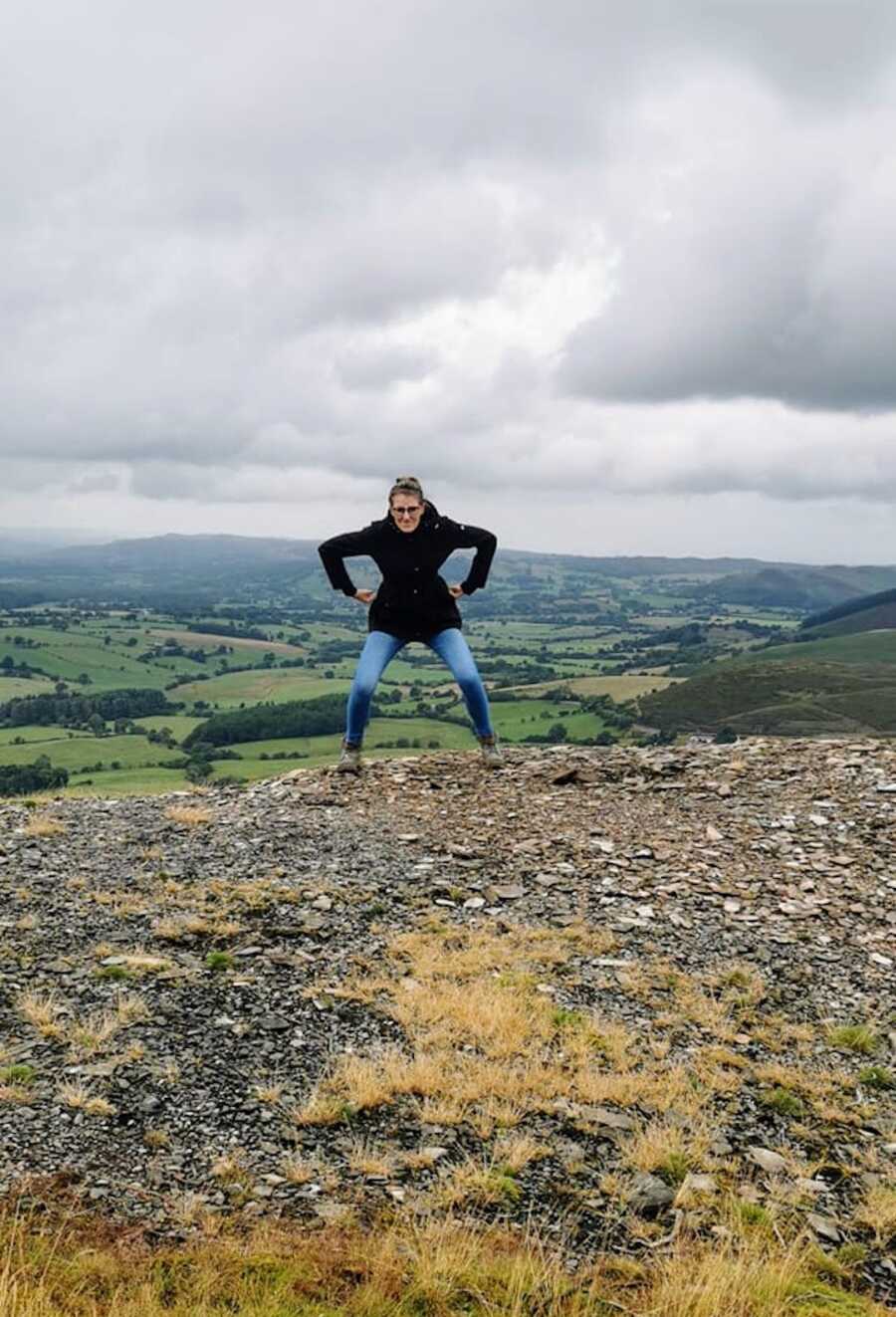 Woman battling FND stands on top mountain and poses