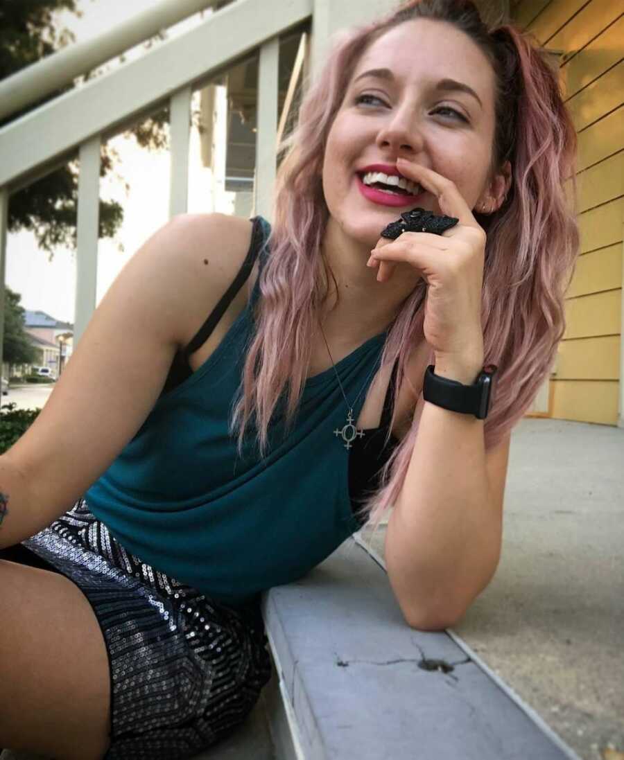 domestic abuse survivor with pink hair sitting on stairs smiling