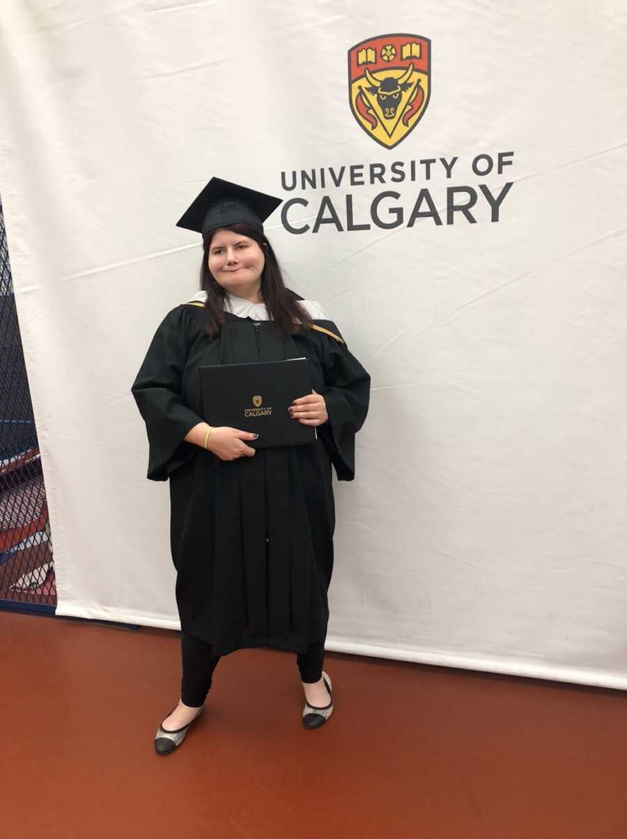 Woman with craniofacial differences poses in graduation attire 