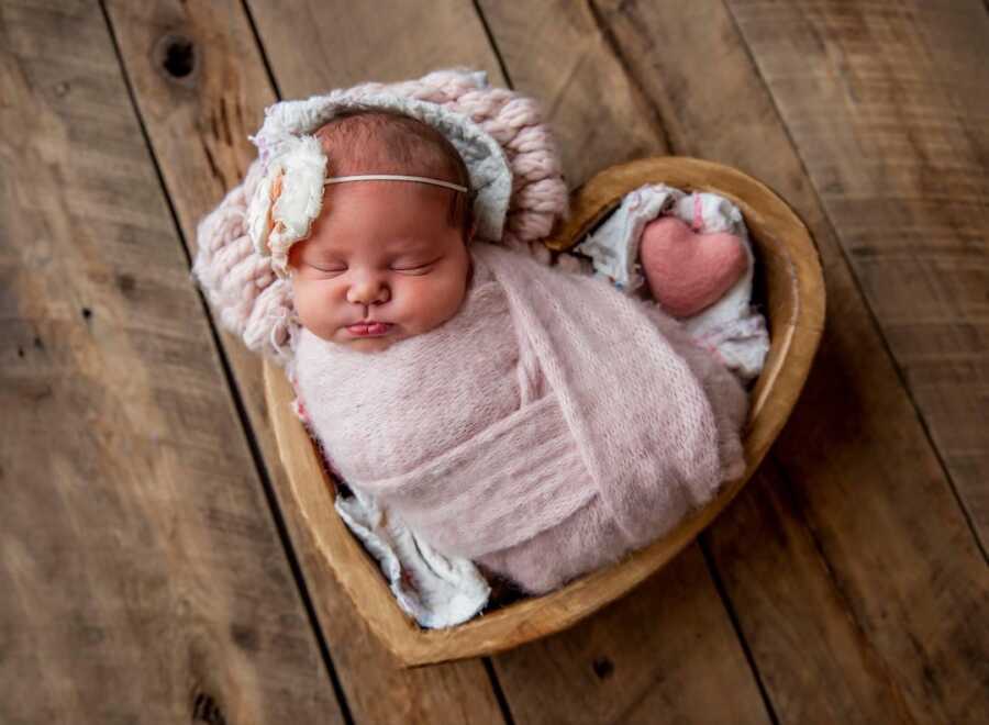 newborn baby girl swaddled in blanket in heart shaped basket