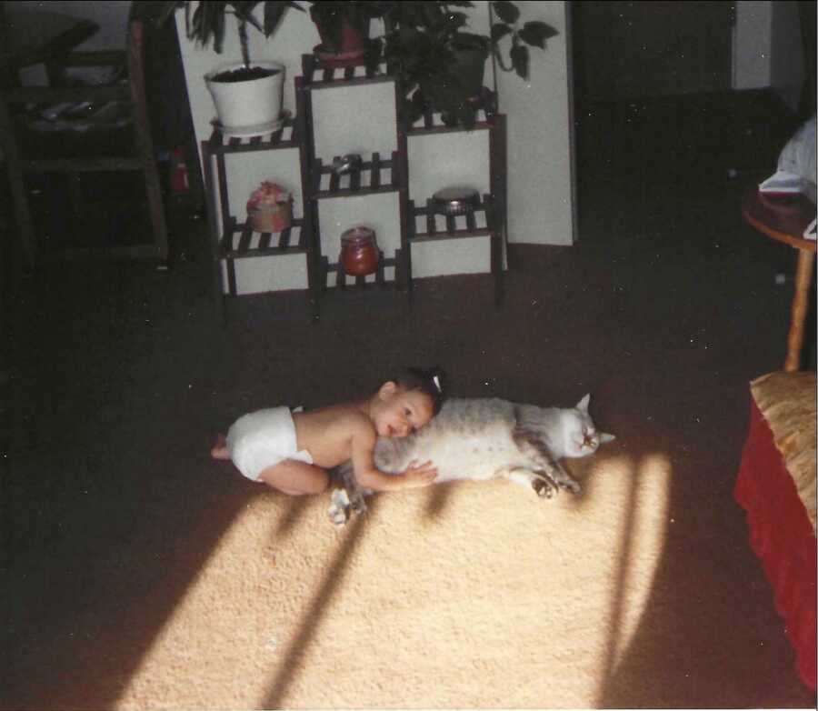 baby laying on cat's back on the floor