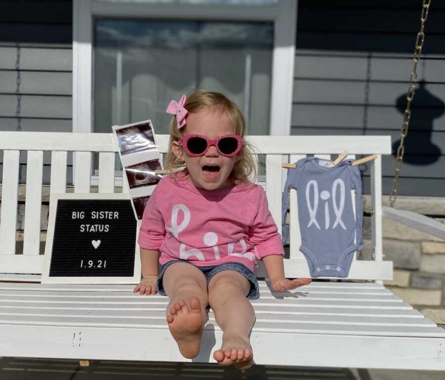 girl sitting on bench for announcement that she is going to be a big sister