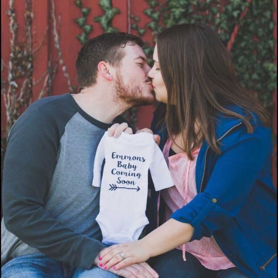 couple holding baby onesie announcing pregnancy while kissing 