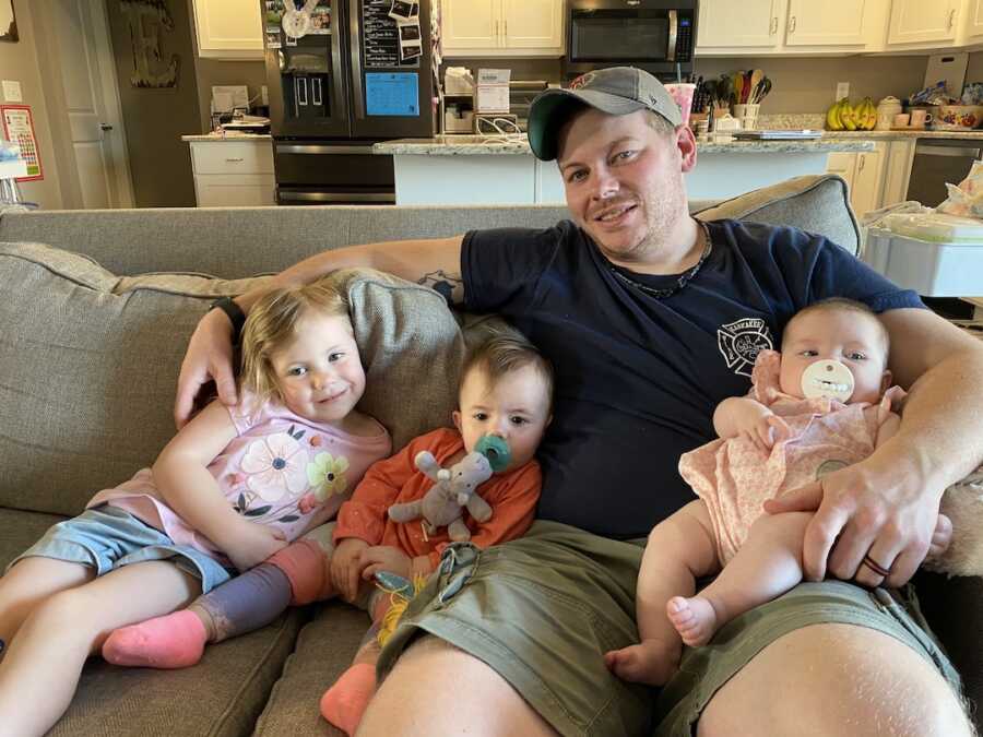 dad sitting on couch with two biological daughter and foster daughter