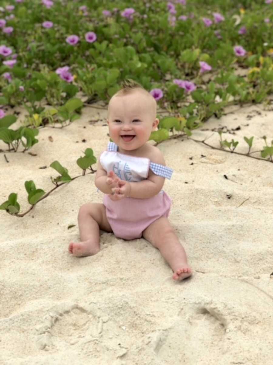 Baby with down syndrome sits on a beach