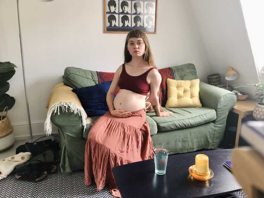 woman with endometriosis sits on couch holding stomach