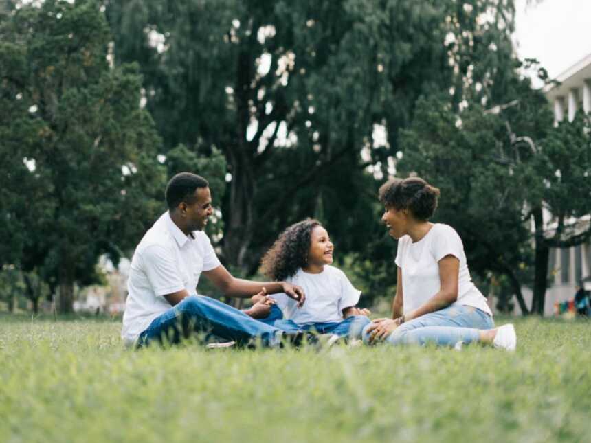 mom dad and daughter sitting sin grass at park enjoying outdoors together