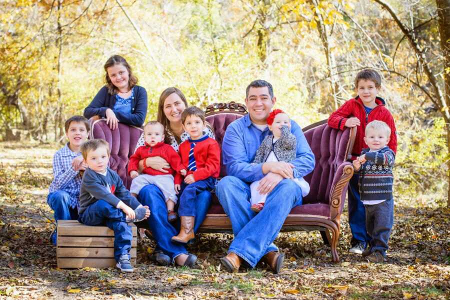 family sits on couch in woods together for Christmas