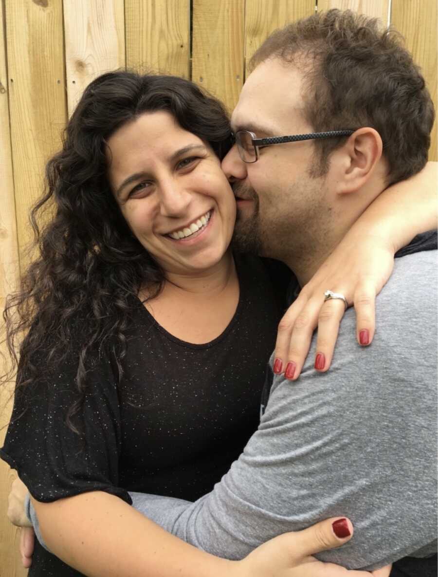 wife puts her arm around her husband who kisses her cheek