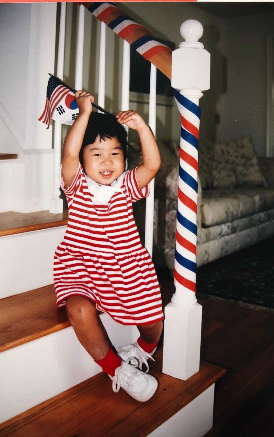 Korean adoptee sitting on steps with American and Korean flags