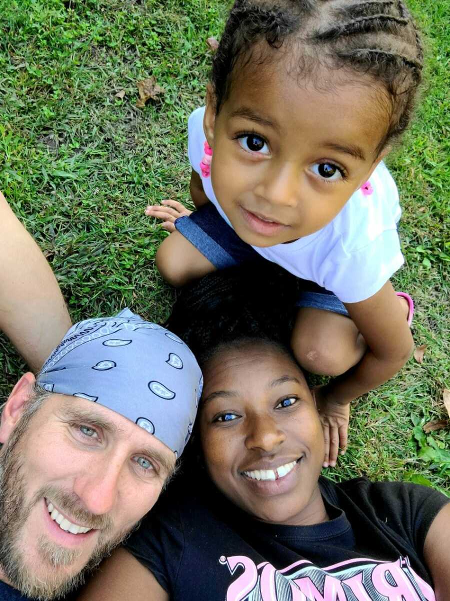 husband laying on grass with wife and daughter wearing blue bandana