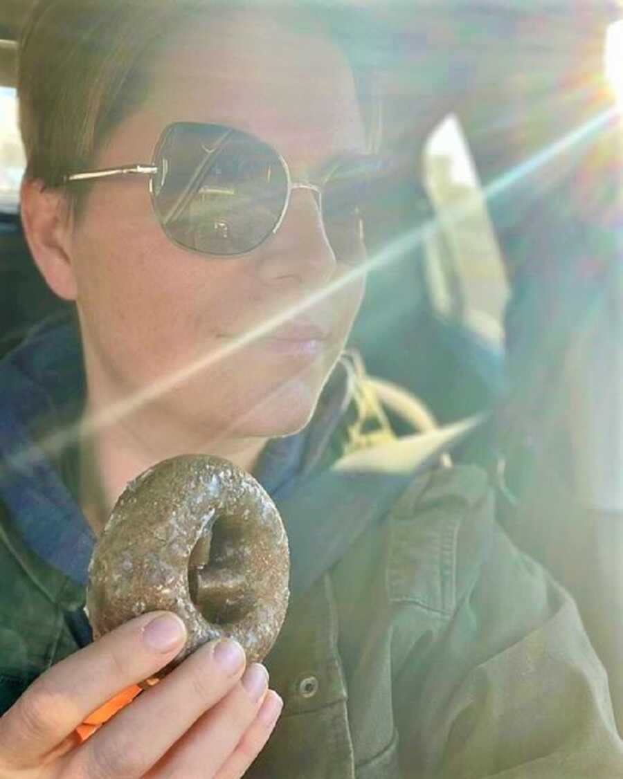 mom driving car while holding donut