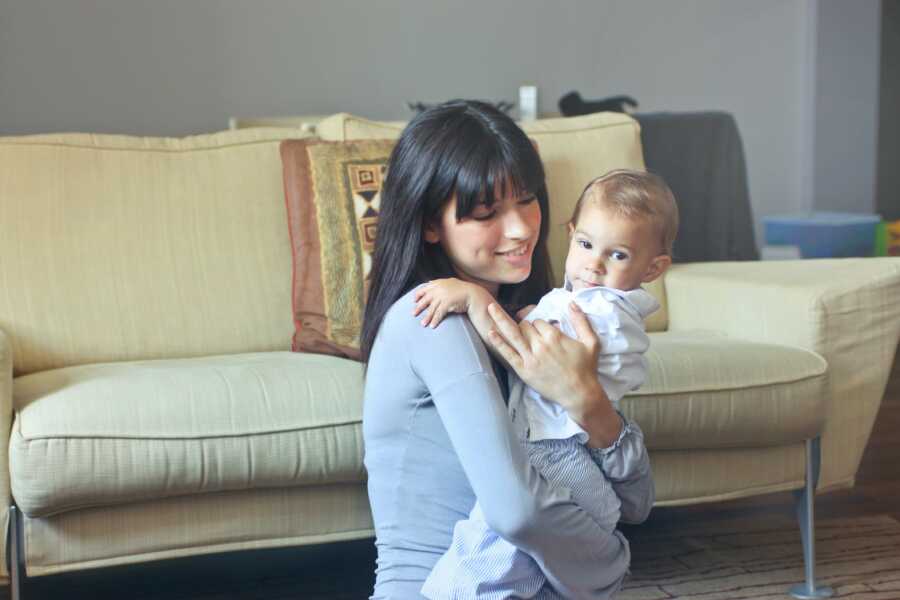 mom holding baby by couch