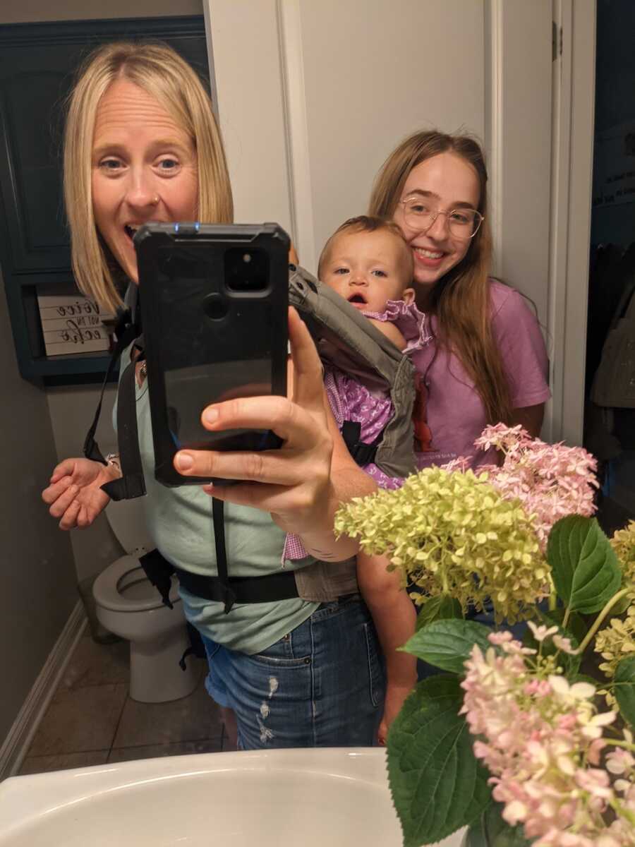 mom takes a mirror selfie with adoptive daughter on her back and biological daughter