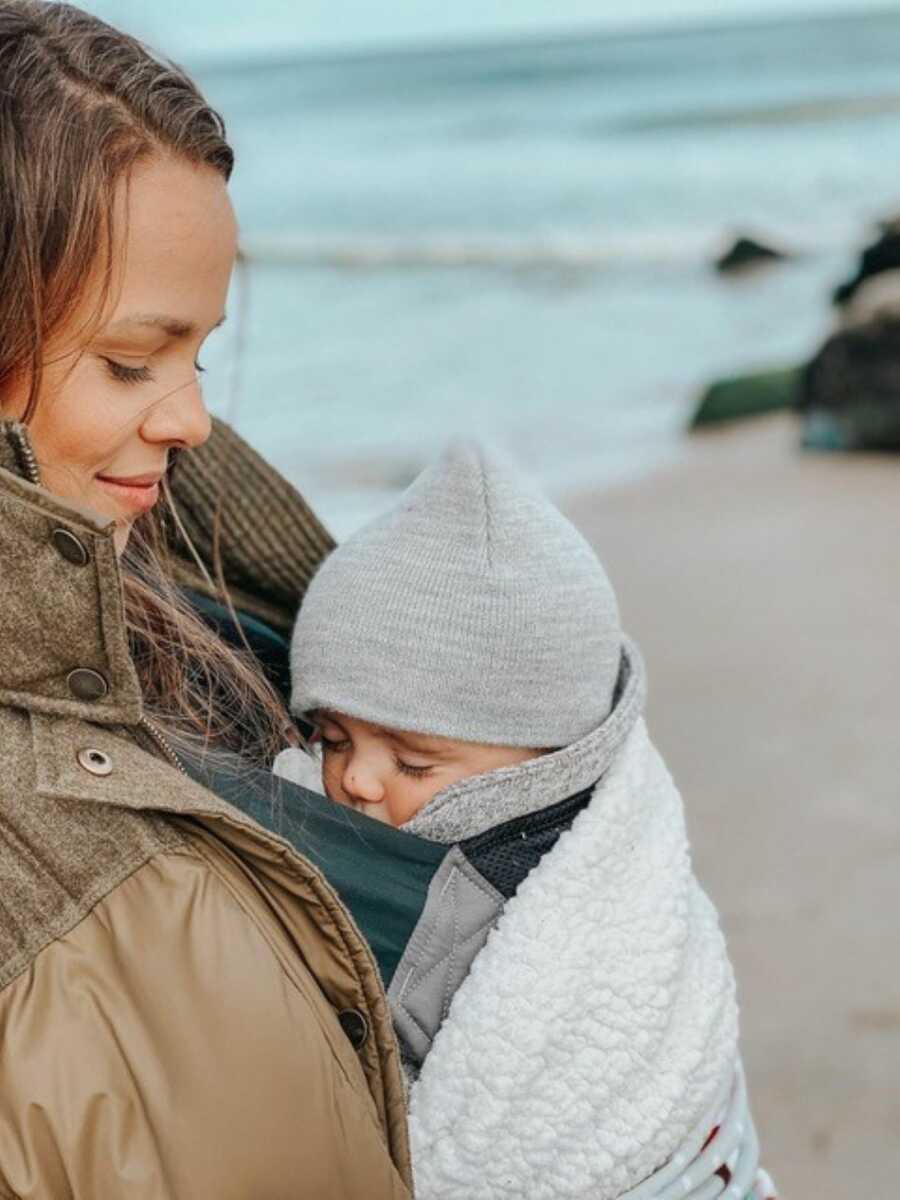 Mother wearing winter coat with her baby swaddled on her chest