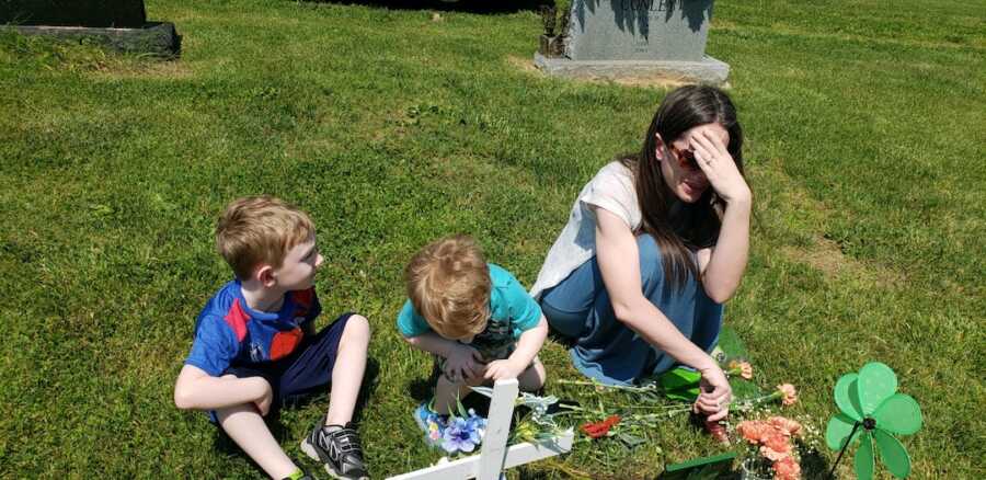 mom sitting with two of her children at her son's grave