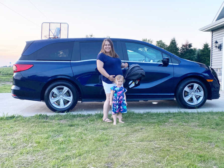 mom standing with biological and foster daughter in front of new minivan