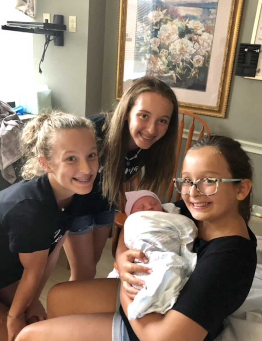 Three older sisters hold their newborn baby brother 