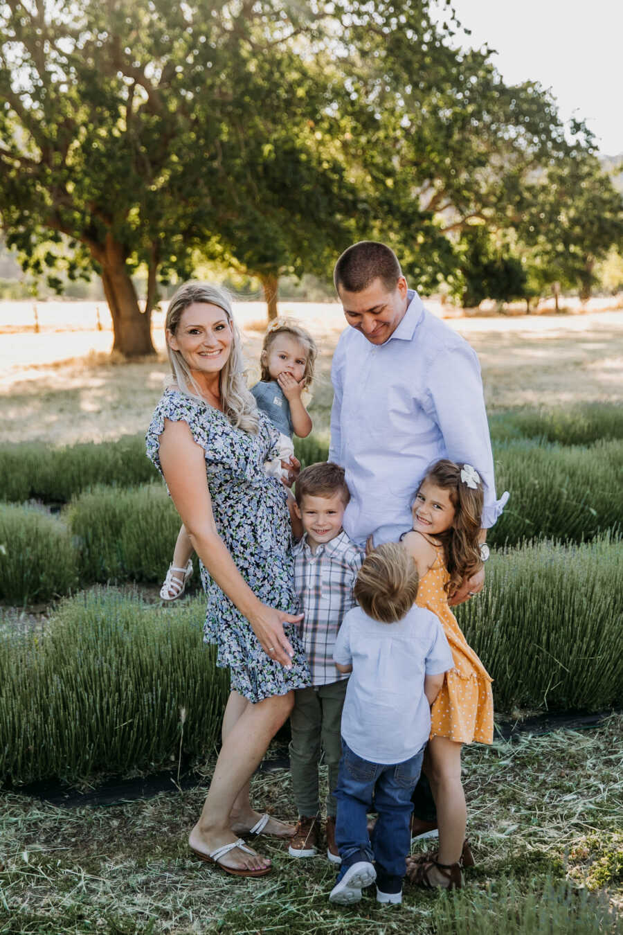 husband and wife stand together smiling with their 4 children