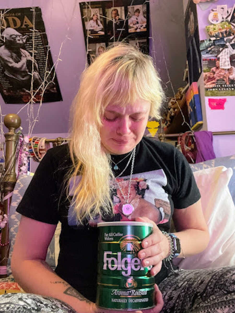 person sitting on floor with ashes of brother in coffee tin