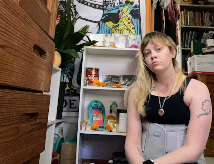 person with chronic illness sitting on the floor in front of a book shelf
