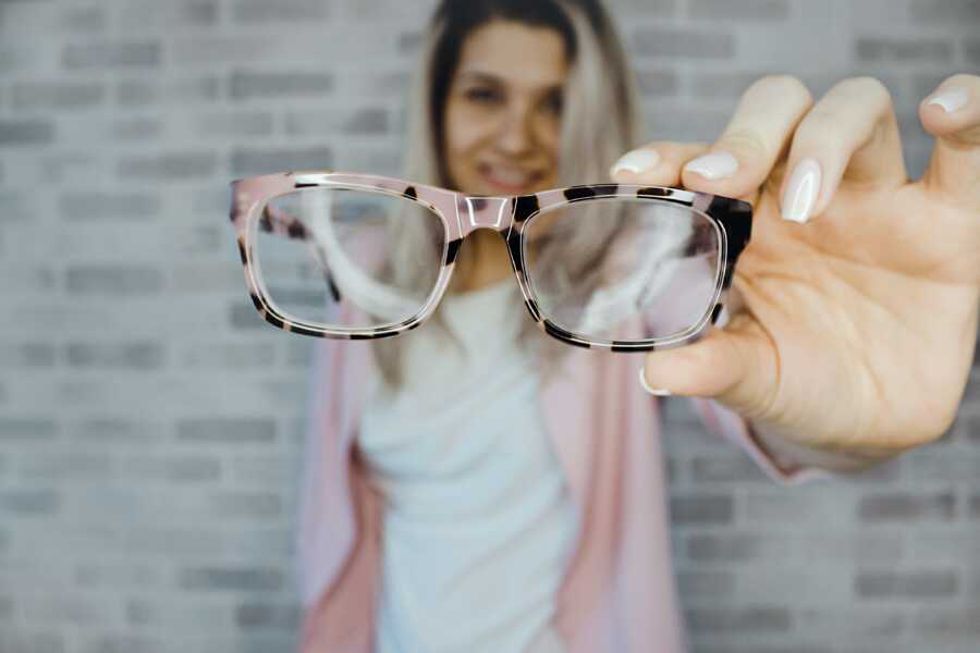 blonde woman in white shirt with pink jacket holding up pink glasses