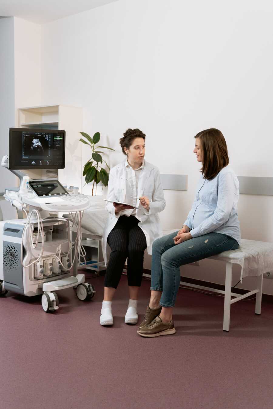 pregnant woman sits in doctors office with doctor