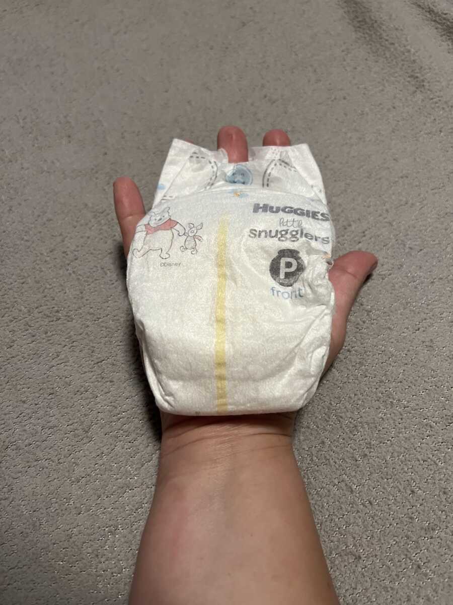 moms hand holding a premie sized diaper