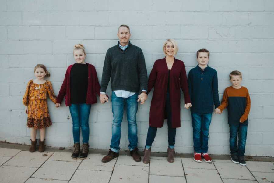 blended family holding hands in a line against a brick wall