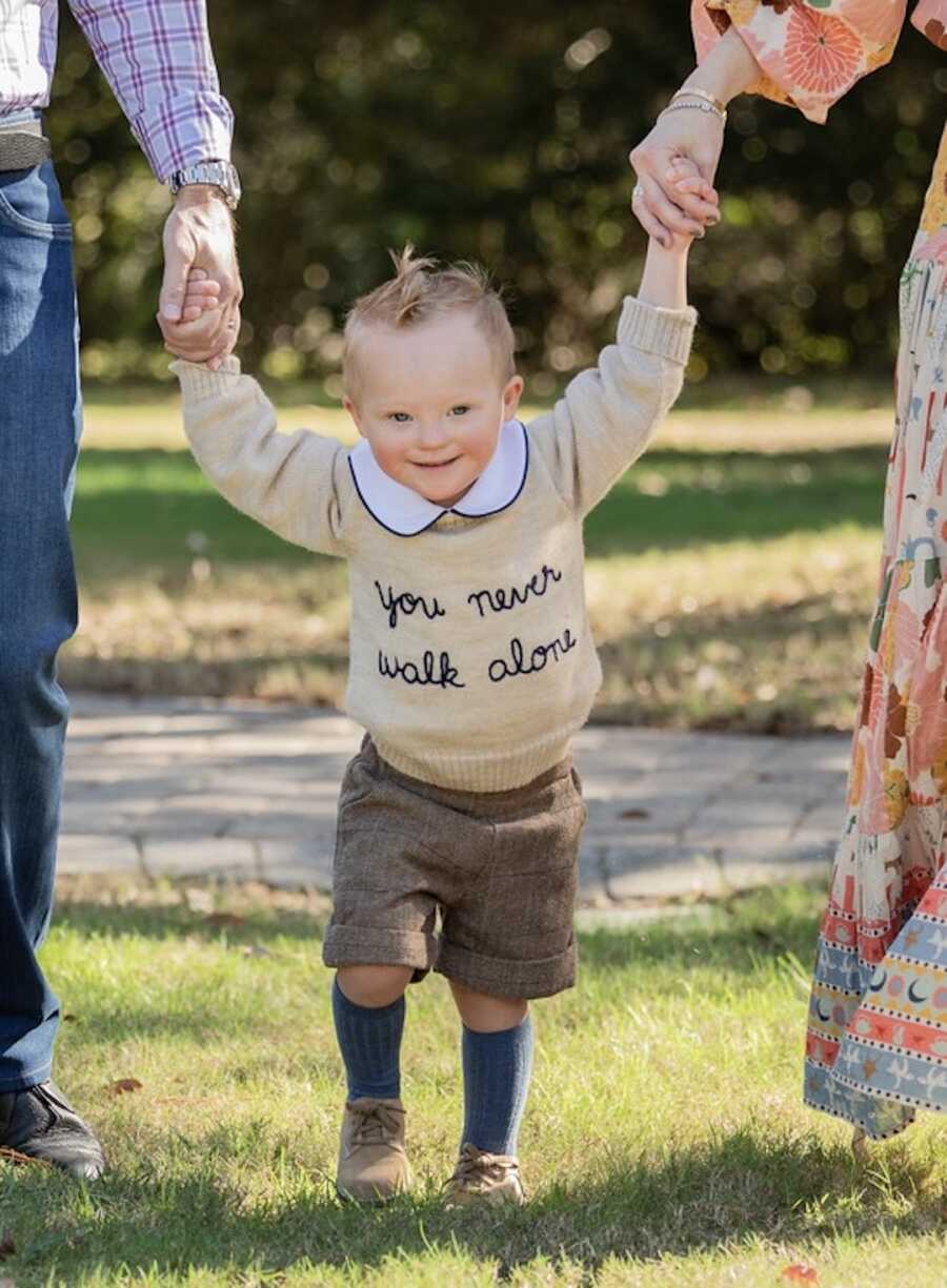 A toddler with down syndrome holds walks while holding parents hands
