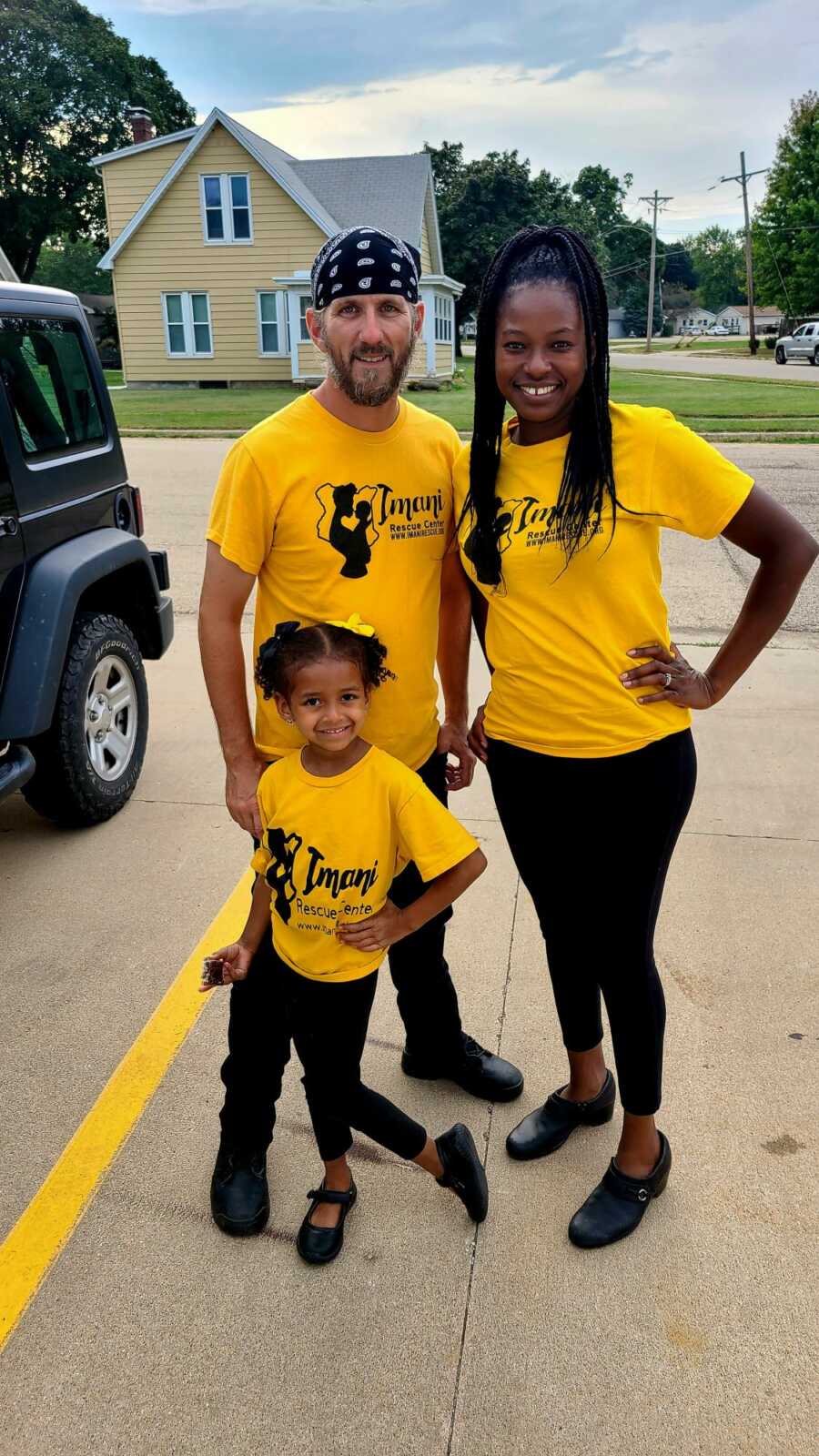Wife, husband, and daughter wearing yellow domestic violence shelter shirts in black pants