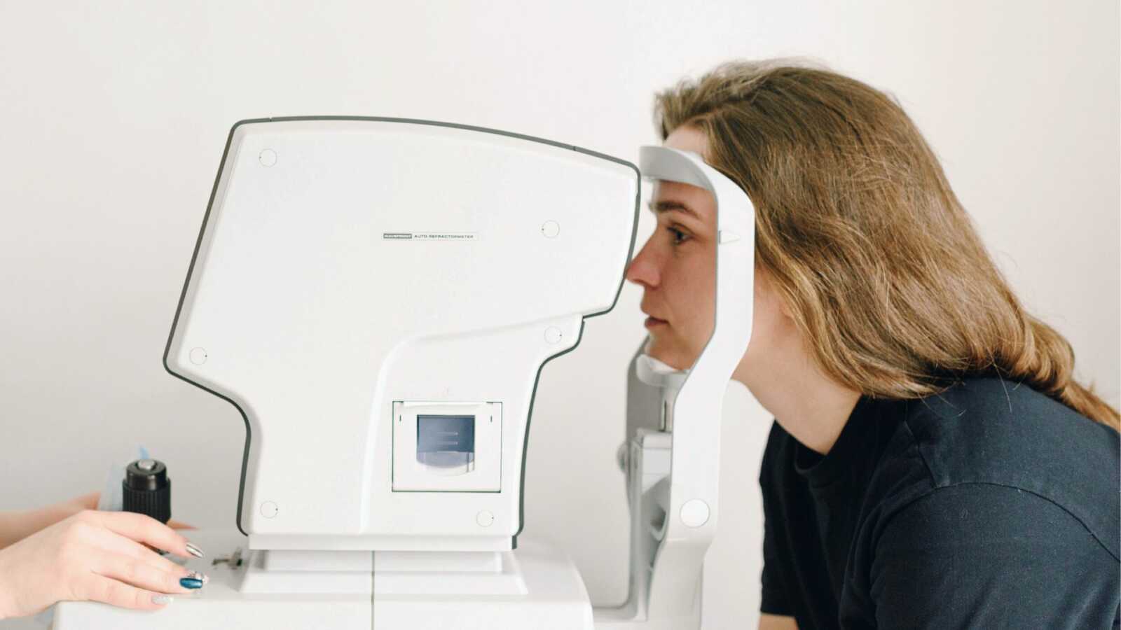 woman sits with head resting on machine at eye doctor