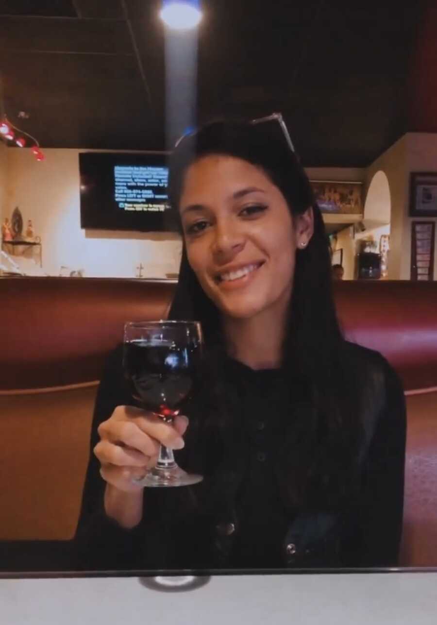 woman sitting in booth holding a glass of wine smiling