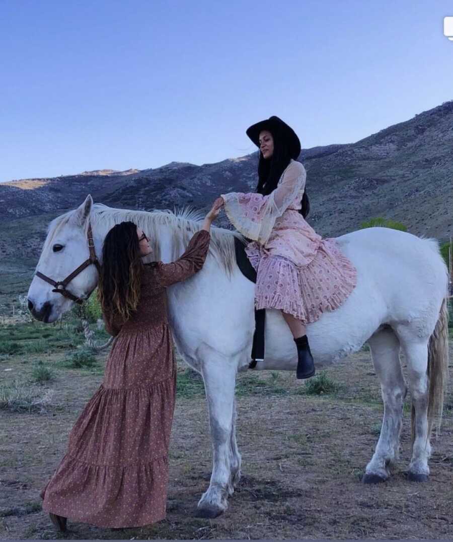 woman sitting on white horse while another woman stands