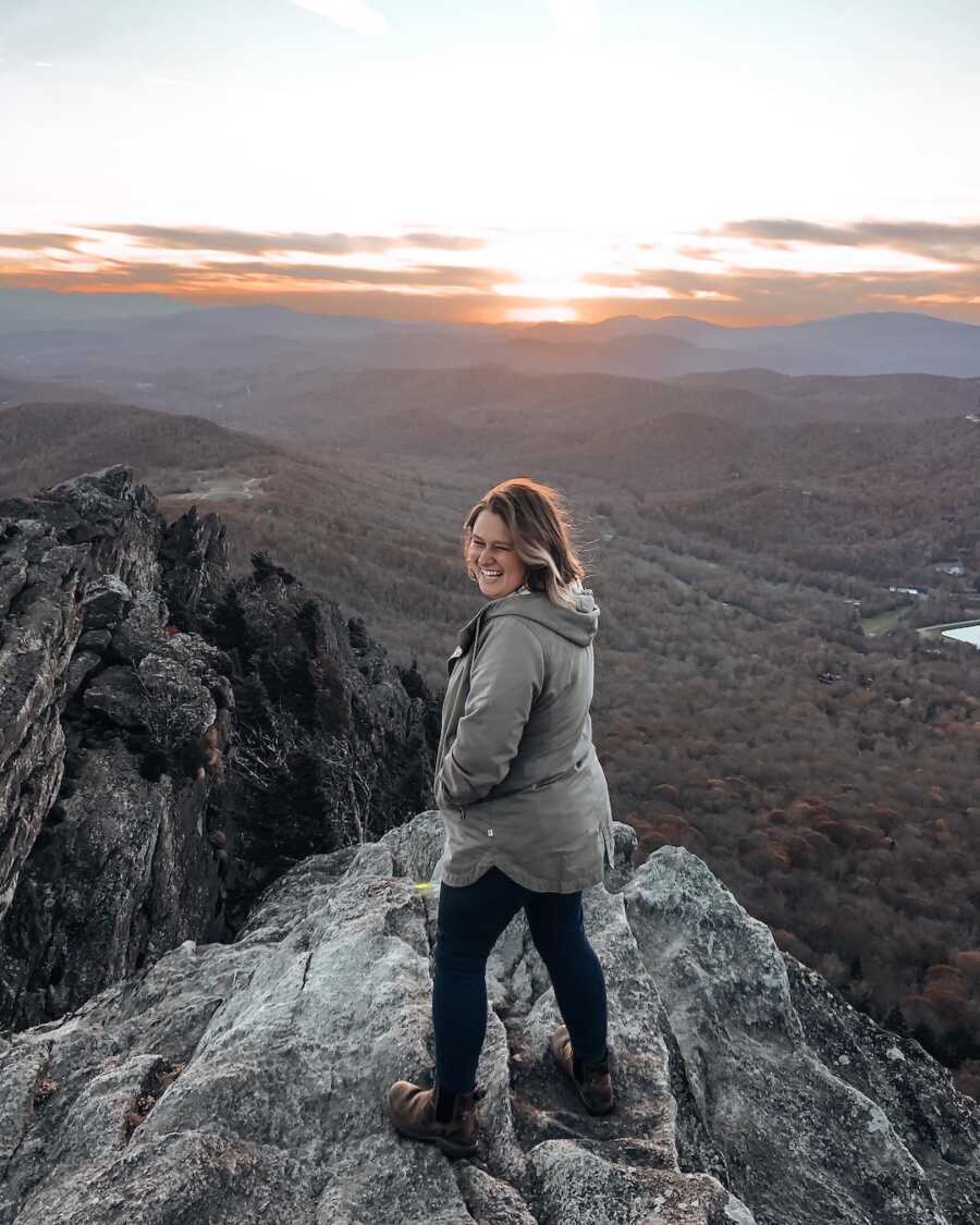 woman looks over shoulder smiling while standing on mountain peak