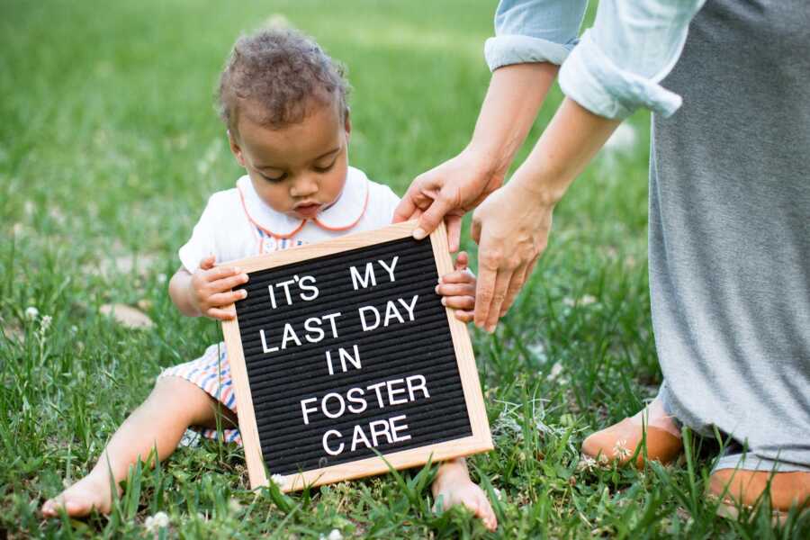 Toddler boy sitting on grass holding sign celebrating his last day in foster care